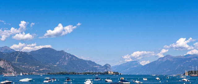 Boats moored on calm blue water below green mountains, with white clouds in a clear blue sky